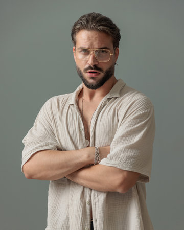cool confident man with beard crossing arms and looking forward in front of grey background in studioの写真素材