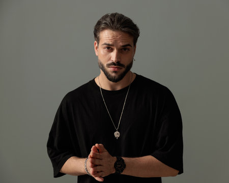 sexy casual man with beard rubbing palms and looking forward in front of dark grey background in studioの写真素材