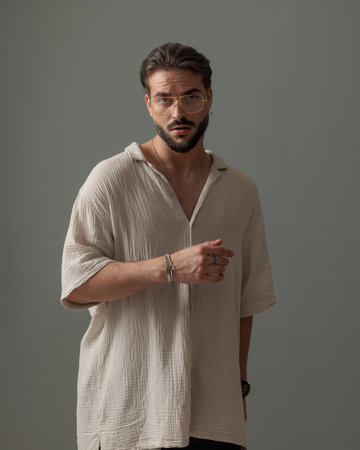 handsome bearded man with glasses looking forward and confident posing in front of grey backgroundの写真素材
