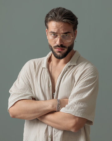 cool fashion man with glasses crossing arms and looking forward in front of grey backgroundの写真素材