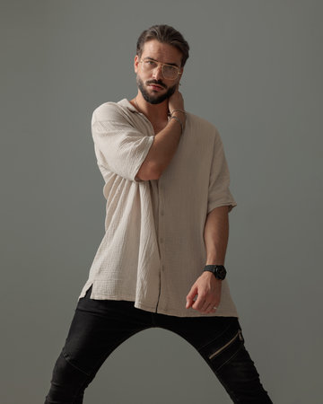 fashion young man with glasses holding arms in a cool pose in front of grey backgroundの写真素材