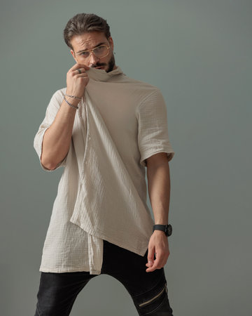 sexy fashion man with glasses covering face with shirt and looking away in front of grey backgroundの写真素材