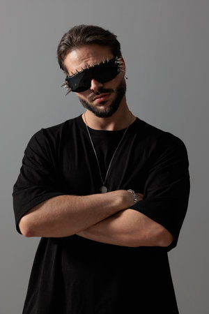 confident bearded guy wearing glasses and folding arms, looking forward and posing in front of grey backgroundの写真素材