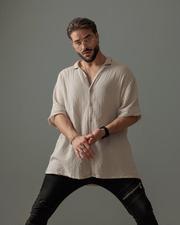 attractive young man holdin arms in fashion pose and looking forward in front of grey backgroundの写真素材