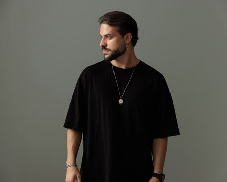 confident cool man in black t-shirt looking to side and posing in front of dark grey background in studioの写真素材