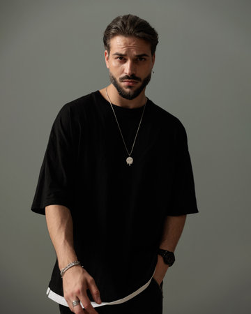 fashion young man in black t-shirt holding hand in pocket and posing in front of dark grey backgroundの写真素材
