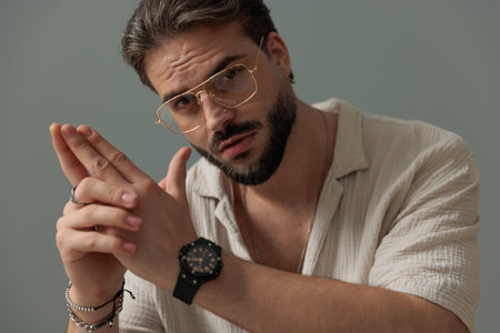casual young man with glasses holding palms together and looking forward in front of grey backgroundの写真素材