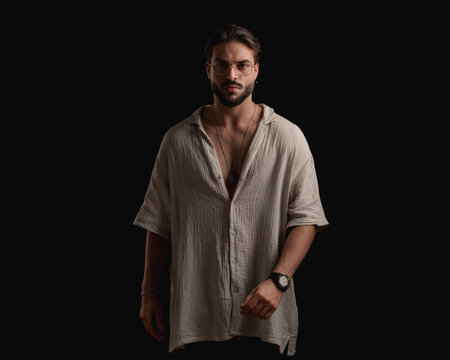 portrait of sexy young man with beard wearing glasses and looking forward in front of black backgroundの写真素材