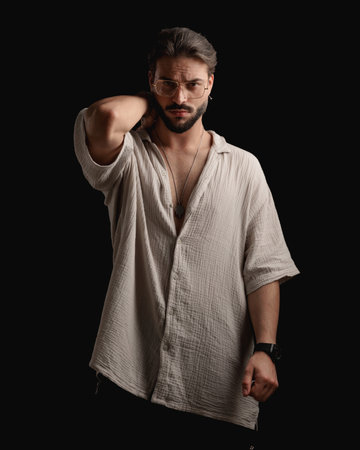 sexy young man with glasses holding hand behind neck and posing in front of black backgroundの写真素材