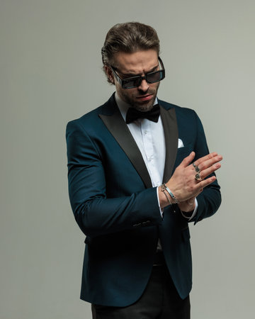 handsome bearded groom with sunglasses looking down and rubbing palms in front of grey backgroundの写真素材
