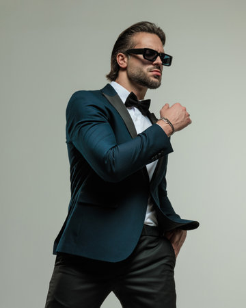 attractive businessman with sunglasses holding hand in pocket and posing in a cool way on grey backgroundの写真素材