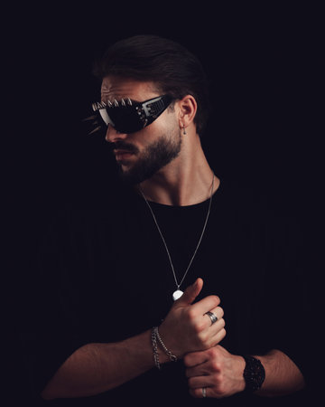 attractive young man with cool sunglasses looking to side and touching palms in front of black backgroundの写真素材