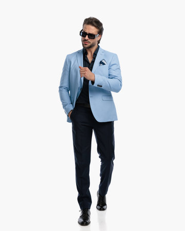 sexy young businessman looking to side and walking with hand in pocket in front of white backgroundの写真素材