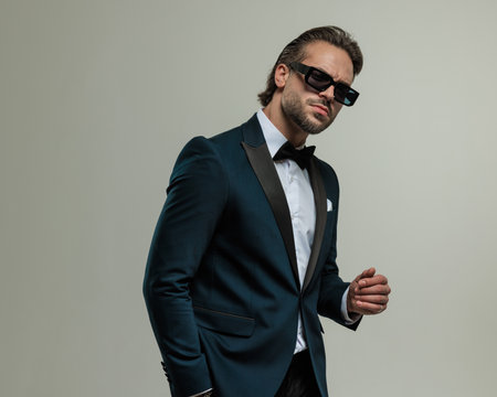 sexy bearded best man with sunglasses holding hands in pockets and posing in front of grey backgroundの写真素材