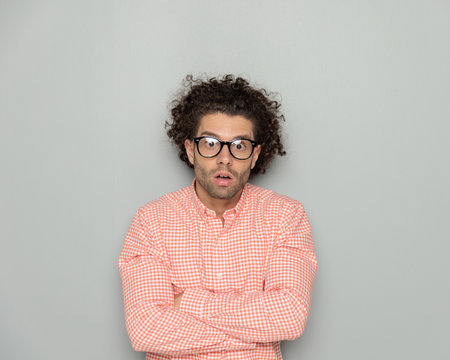 astounded curly hair guy with glasses opening mouth while crossing arms and being shocked in front of grey backgroundの写真素材