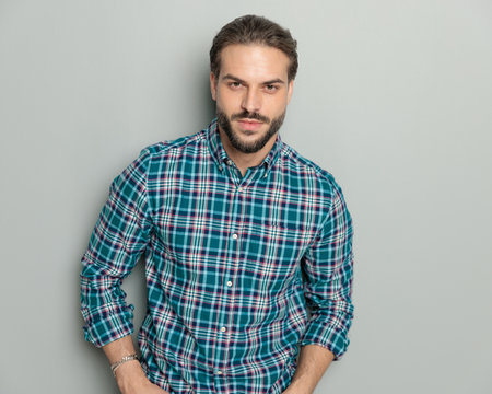 portrait of attractive casual man wearing plaid shirt, looking forward and posing in a confident way on grey backgroundの写真素材