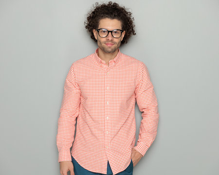 handsome young guy with curly hair holding hand in pocket and smiling while posing in front of grey background in studioの写真素材
