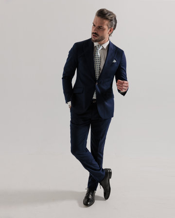sexy businessman with beard holding hand in pocket and looking to side in front of grey backgroundの写真素材