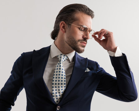 portrait of confident elegant man looking down side and arranging eyeglasses in front of grey backgroundの写真素材