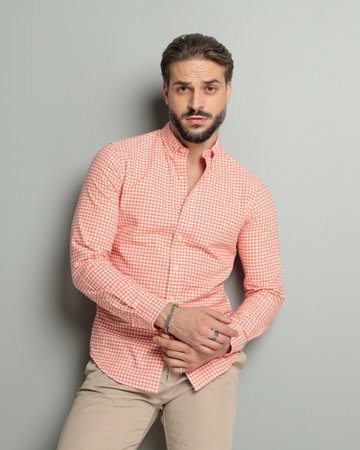 sexy guy with beard holding arms in fashion pose and posing in a cool way in front of grey backgroundの写真素材