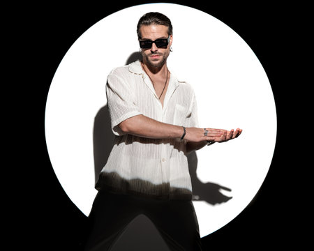 portrait of sexy bearded man with sunglasses looking forward and rubbing palms to side in front of white background in studioの写真素材