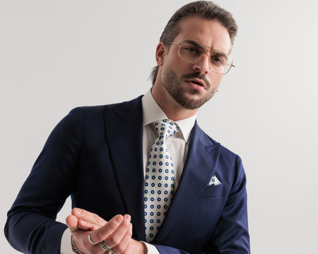 portrait of sexy elegant man with glasses looking forward and rubbing palms in front of grey backgroundの写真素材