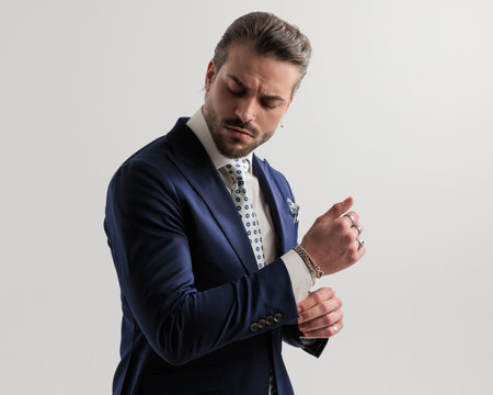 side view of sexy fashion man in navy blue suit suit looking down while fixing sleeves in front of grey backgroundの写真素材