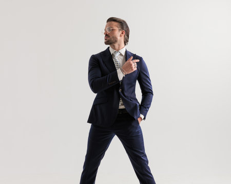 confident businessman with glasses looking to side and holding hand in pocket while posing in a cool way on grey backgroundの写真素材