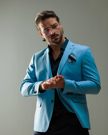 portrait of attractive young man with glasses looking to side and rubbing palms in front of grey backgroundの写真素材