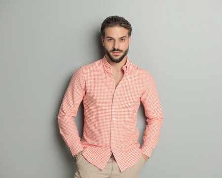sexy bearded guy in plaid shirt holding hands in pockets and posing while looking forward in front of grey backgroundの写真素材