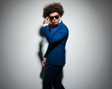 side view of fashion high class businessman adjusting sunglasses and being cool in front of grey backgroundの写真素材
