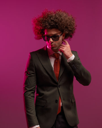 confused elegant man with long curly hair touching neck, looking down side and thinking in front of pink backgroundの写真素材