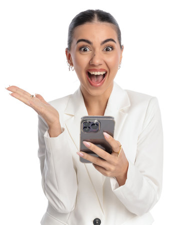 excited young woman holding mobile, reading good news and being extremely happy in front of white backgroundの写真素材