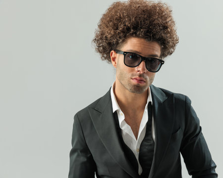 portrait of handsome elegant man with sunglasses looking forward and posing in front of grey backgroundの写真素材