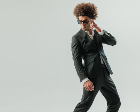 sexy elegant man with afro hair looking to side and adjusting sunglasses while posing in a cool way on grey backgroundの写真素材