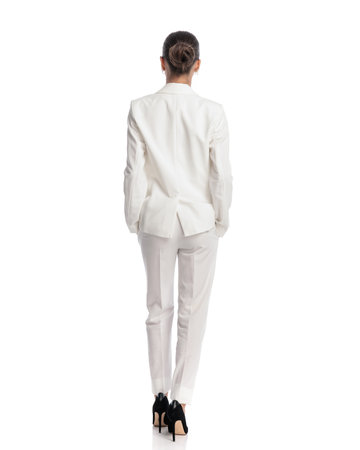 back view of sexy woman in white suit holding arms in pockets and standing in front of white backgroundの写真素材