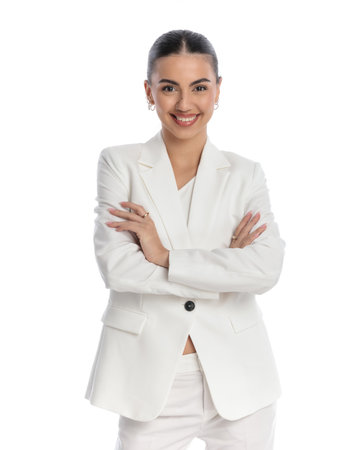 fashion young woman in white suit with bun hair crossing arms and smiling while confidently posing in front of white backgroundの写真素材