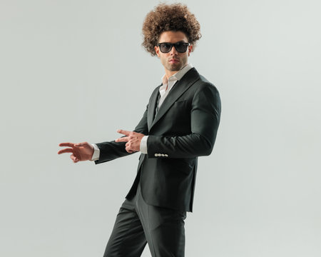 elegant businessman in black tuxedo with sunglasses pointing fingers to side and looking forward in front of grey backgroundの写真素材