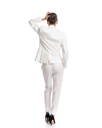 confused businessman with bun hair in white suit scratching head and thinking of ways to solve difficult problems while walking with hand in pocket on white backgroundの写真素材