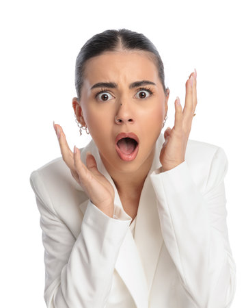 astounded young woman opening mouth, holding hands up and being shocked by the news in front of white backgroundの写真素材