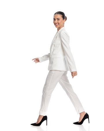 full body picture of happy elegant young woman in white suit walking and being happy in front of white backgroundの写真素材