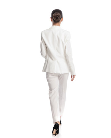 rear view of elegant fashion model with bun hair in elegant white suit walking in front of white backgroundの写真素材
