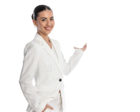 confident young businesswoman happily inviting and welcoming while posing with hand in pocket on white backgroundの写真素材
