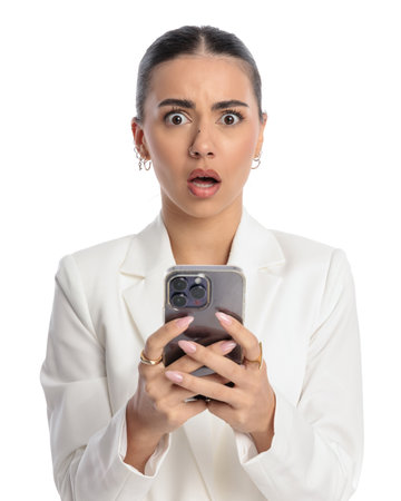 shocked young lady holding telephone and reading astonishing messages in front of white backgroundの写真素材