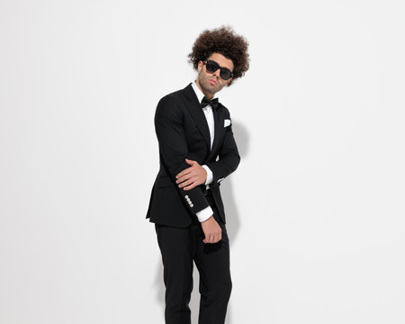 cool young man with sunglasses holding arms in fashion pose and posing in front of grey backgroundの写真素材