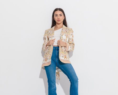 attractive hippie girl looking forward and adjusting paisley print jacket in front of grey backgroundの写真素材