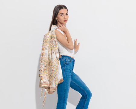 side view of beautiful smart casual girl with jacket on shoulder posing in front of grey backgroundの写真素材