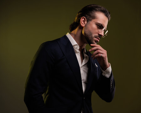 portrait of thoughtufl elegant businessman looking to side, touching chin and thinking in front of yellow backgroundの写真素材