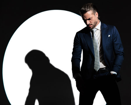 sexy elegant businessman looking down while holding hands in pockets in front of white background with spotlight onの写真素材