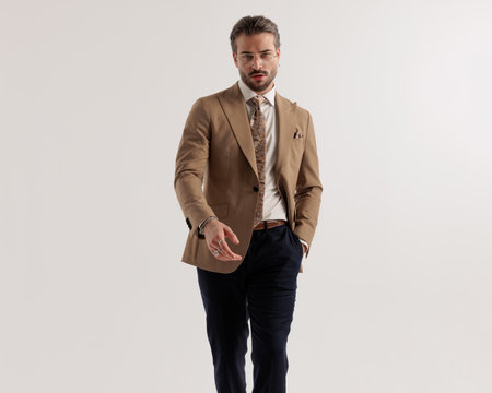 cool fashion man with glasses walking with hands in pockets in front of grey background in studioの写真素材